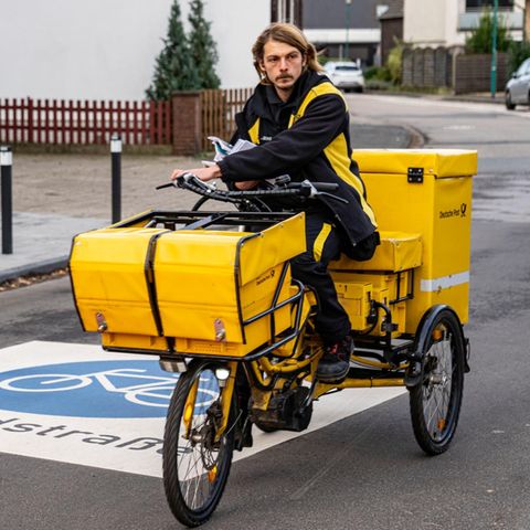 Briefträger fährt die Post auf dem dreirädrigen Lastenfahrrad aus