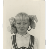 Ein Porträt der 9-jährigen Irina. Sie trägt ein schickes Kleid, die Haare mit Schleifen darin sind zu Zöpfen geflochten