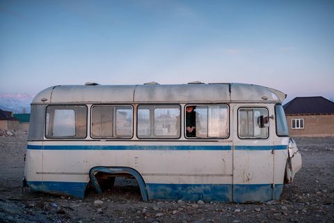 Ein alter Bus ohne Räder, darin spielt ein jugendliches Mädchen in der Abenddämmerung