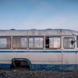 Ein alter Bus ohne Räder, darin spielt ein jugendliches Mädchen in der Abenddämmerung