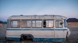 Ein alter Bus ohne Räder, darin spielt ein jugendliches Mädchen in der Abenddämmerung