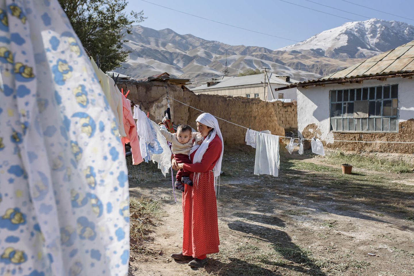 Rückkehrer Eine Mutter hält ihren Sohn im Arm. Sie stehen auf dem Hof, über den eine Wäscheleine gespannt ist. Dahinter sind Berge
