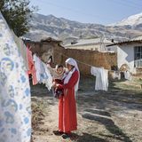 Eine Mutter hält ihren Sohn im Arm. Sie stehen auf dem Hof, über den eine Wäscheleine gespannt ist. Dahinter sind Berge