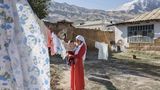 Eine Mutter hält ihren Sohn im Arm. Sie stehen auf dem Hof, über den eine Wäscheleine gespannt ist. Dahinter sind Berge