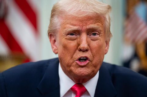 Donald Trump sitzt vor einer US-Flagge und spricht