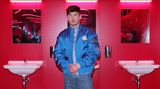 "Saltburn"-Star Barry Keogahn in einer blauen Jacke vor rot gekachelter Showkulisse