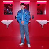 "Saltburn"-Star Barry Keogahn in einer blauen Jacke vor rot gekachelter Showkulisse