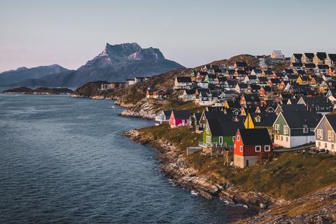 Nuuk, Grönland: Bunte Häuser stehen aufreiht an den Klippen am Meer. Die Sonne geht unter.