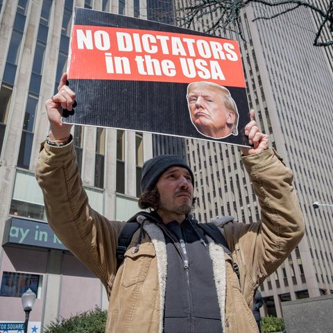 Ein Mitglied einer Aktivistengruppe steht mit einem Schild gegen Donald Trump vor einem Hochhaus