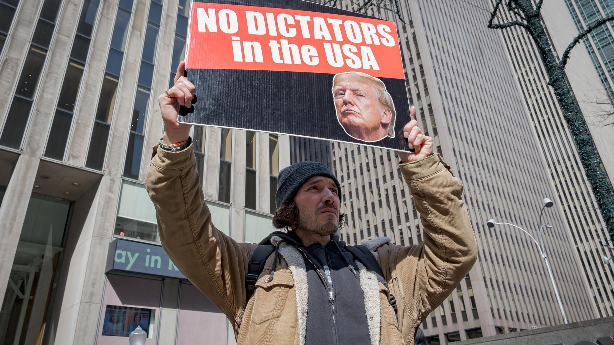 Ein Mitglied einer Aktivistengruppe steht mit einem Schild gegen Donald Trump vor einem Hochhaus