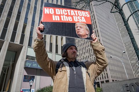 Ein Mitglied einer Aktivistengruppe steht mit einem Schild gegen Donald Trump vor einem Hochhaus