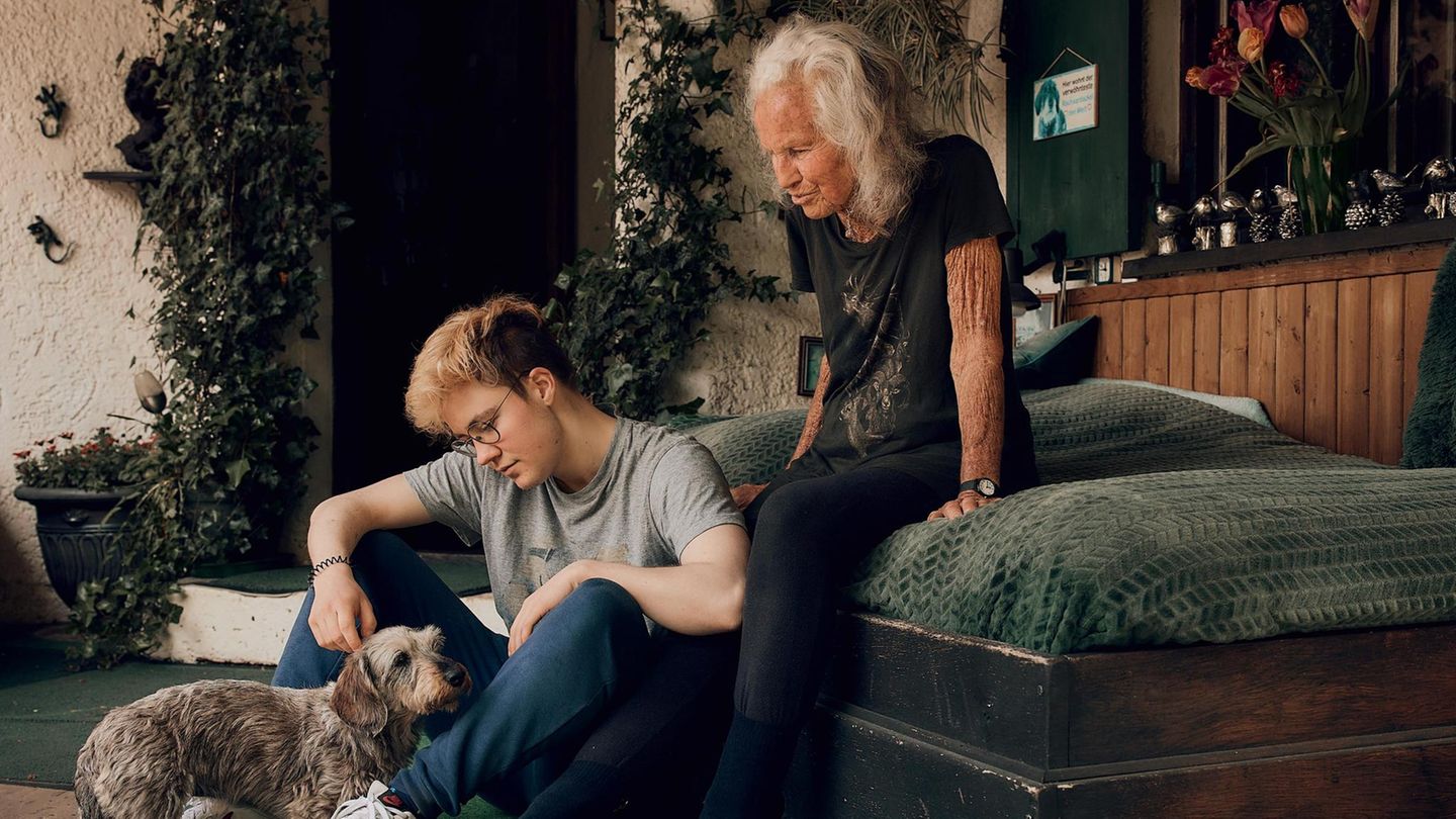 Lennart streichelt einen Dackel, während seine Oma hinter ihm auf dem Bettt sitzt