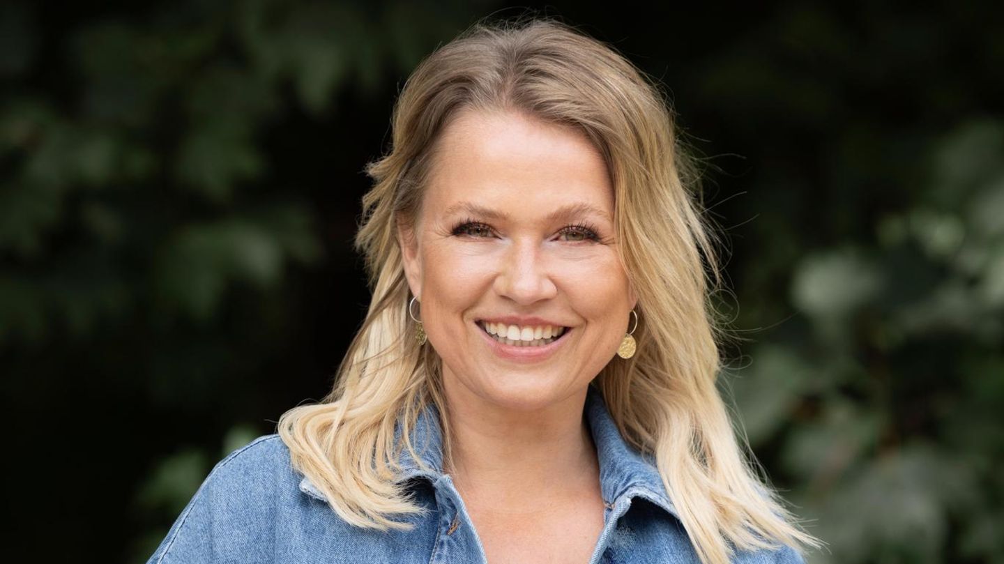 Nova Meierhenrich Autorin Moderatorin 2024 Nova Meierhenrich lächelnd vor einer Hecke