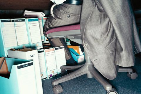 Ein Mann sitzt am Schreibtisch im Anzug, Ordner auf dem Boden