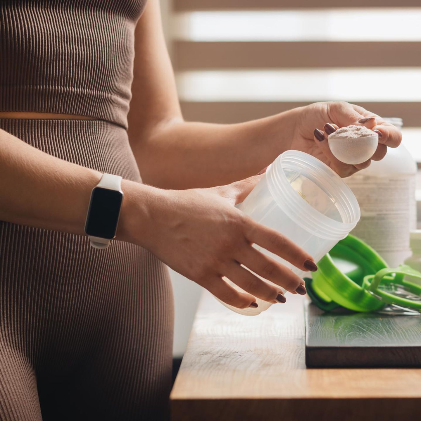 Eine Frau schüttet Kreatin Pulver in einen Drink.