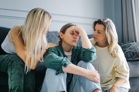 drei Frauen in einem Wohnzimmer, zwei Frauen trösten die dritte Frau in der Mitte