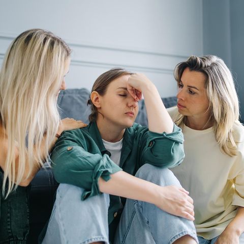 drei Frauen in einem Wohnzimmer, zwei Frauen trösten die dritte Frau in der Mitte
