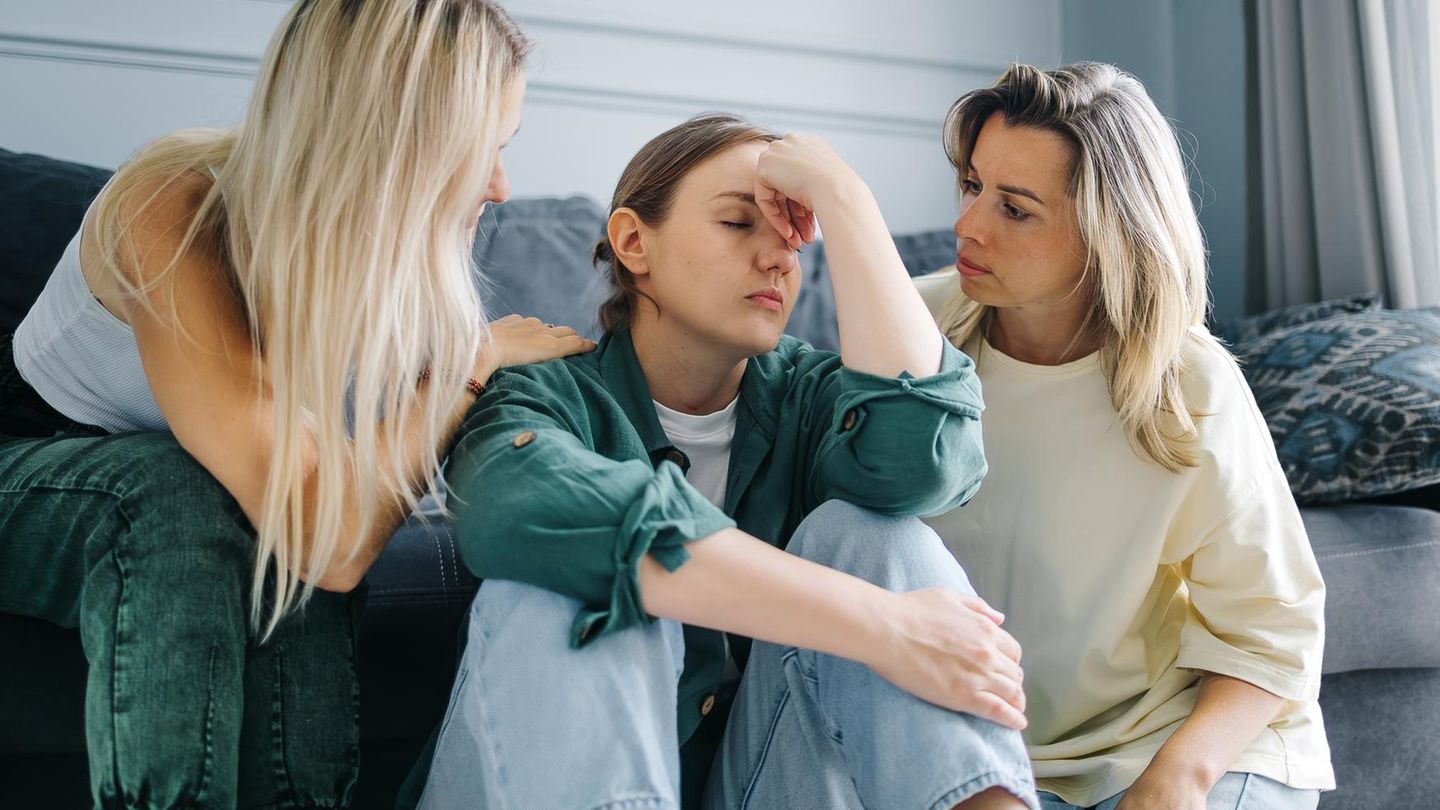 drei Frauen in einem Wohnzimmer, zwei Frauen trösten die dritte Frau in der Mitte