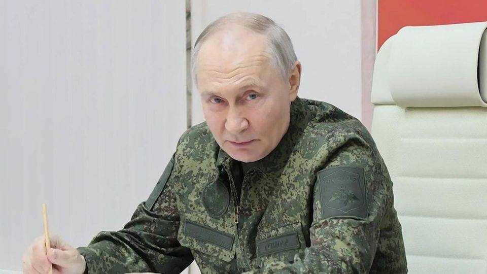 Wladimir Putin sitzt in einem Camouflage-Anzug an einem Schreibtisch