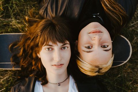Zwei junge Frauen der Gen Z liegen auf dem Rücken und schauen in die Kamera
