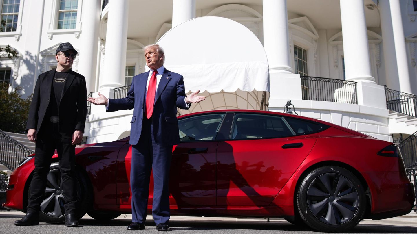 Elon Musk und Donald Trump stehen vor einem roten Tesla