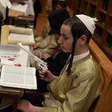 Jüdische ultraorthodoxe Männer und Kinder, von denen einige Kostüme tragen, lesen in der Synagoge