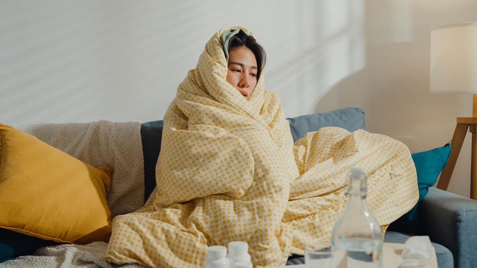  Eine Frau sitzt auf dem Sofa und ist in eine Decke eingehüllt