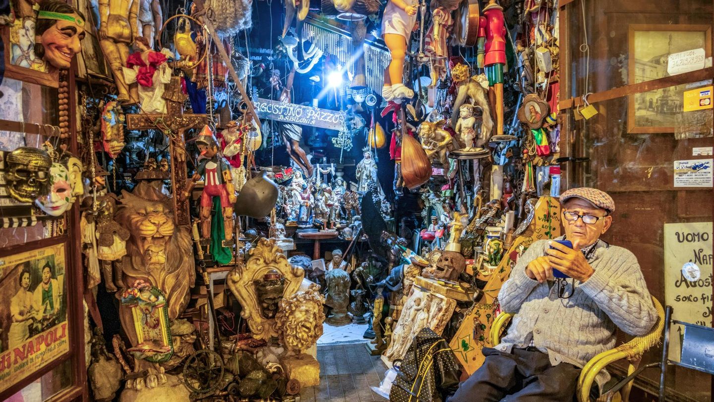 Ein alter Mann sitzt vor einem dicht gefüllten Altstadtladen in Neapel