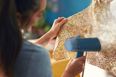 Frau glättet glitzerndes Kleidungsstück mit einem Dampfglätter