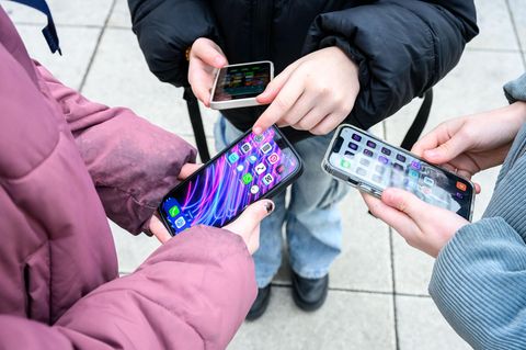Drei junge Schüler stehen mit Handys in ihren Händen zusammen