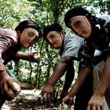 Versteckt hinter traditionellen indigenen Tanzmasken üben diese Kinder das Schmeißen von Steinen