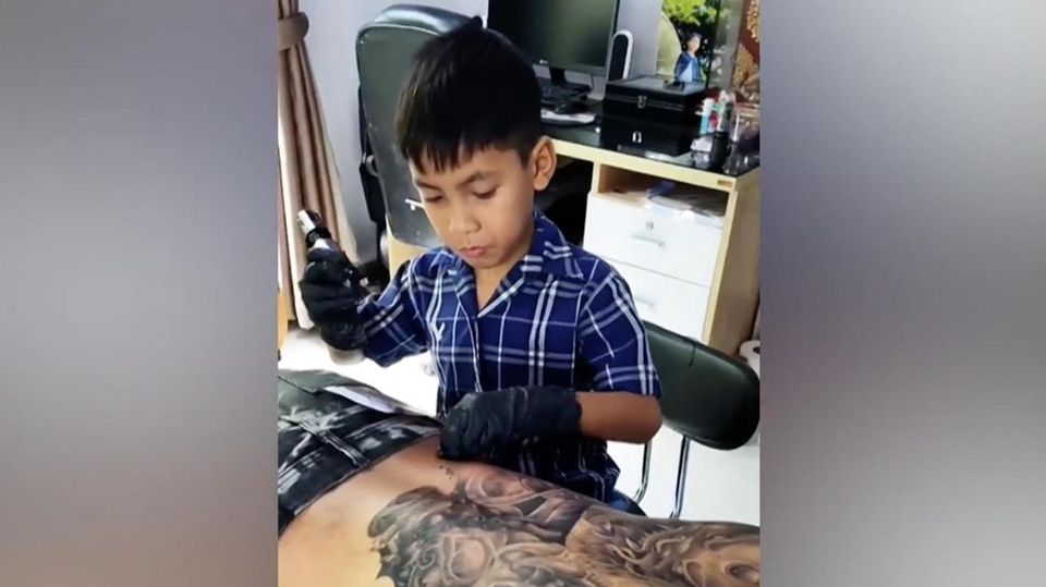 Der neunjährige Napat Mitmakorn tätowiert den Rücken eines Mannes großflächig
