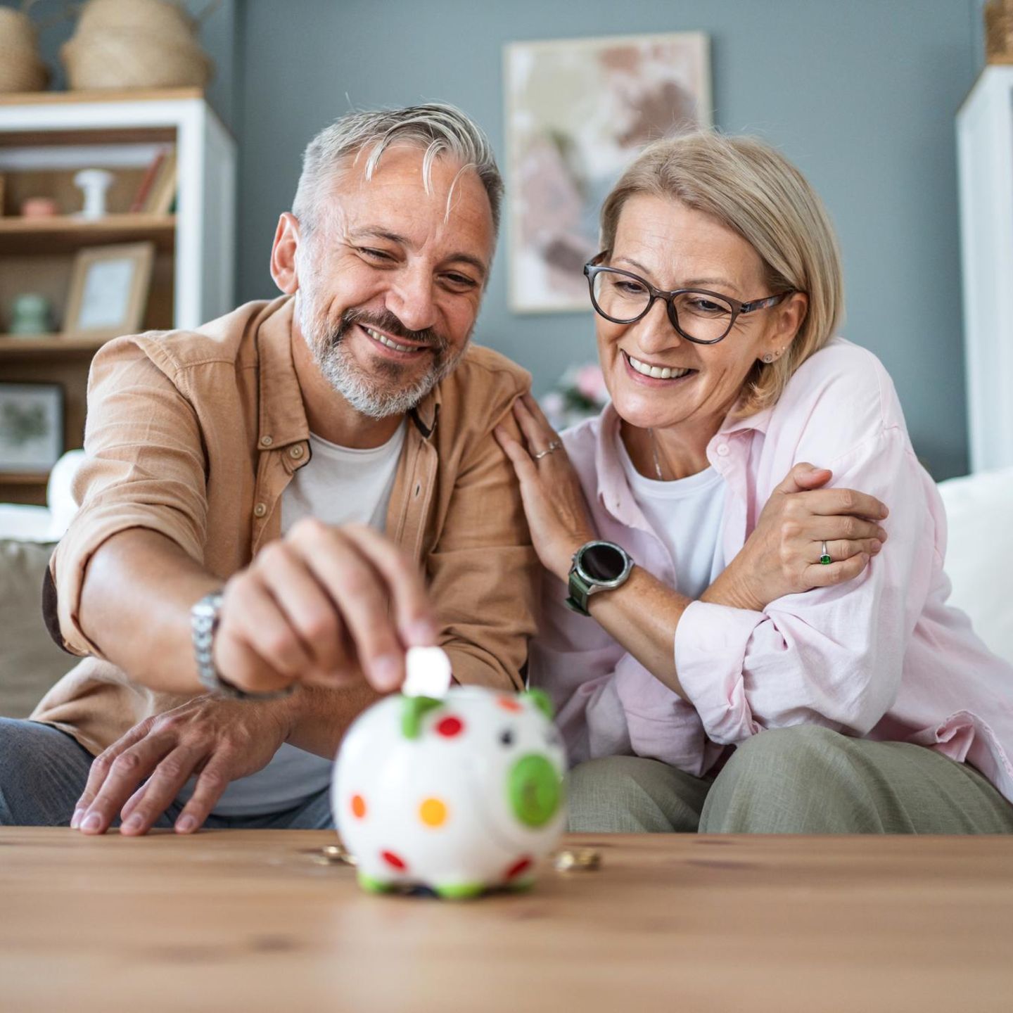 Rente: Zwei ältere Menschen stecken einen Euro in ein Sparschwein