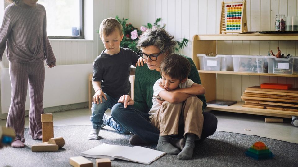 eine Erzieherin liest drei Kindern aus einem Buch vor
