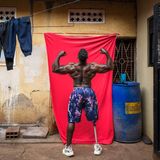 Bodybuilder Tamale Safalu steht vor einer Wand und hebt die Arme nach oben.