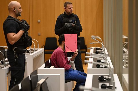 Der mutmaßliche Messerattentäter von Mannheim sitzt im Gerichtssaal und verdeckt sein Gesicht mit einem Ordner.