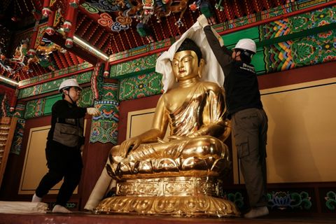 Arbeiter verhüllen eine Buddha-Statue mit Brandschutzdecken