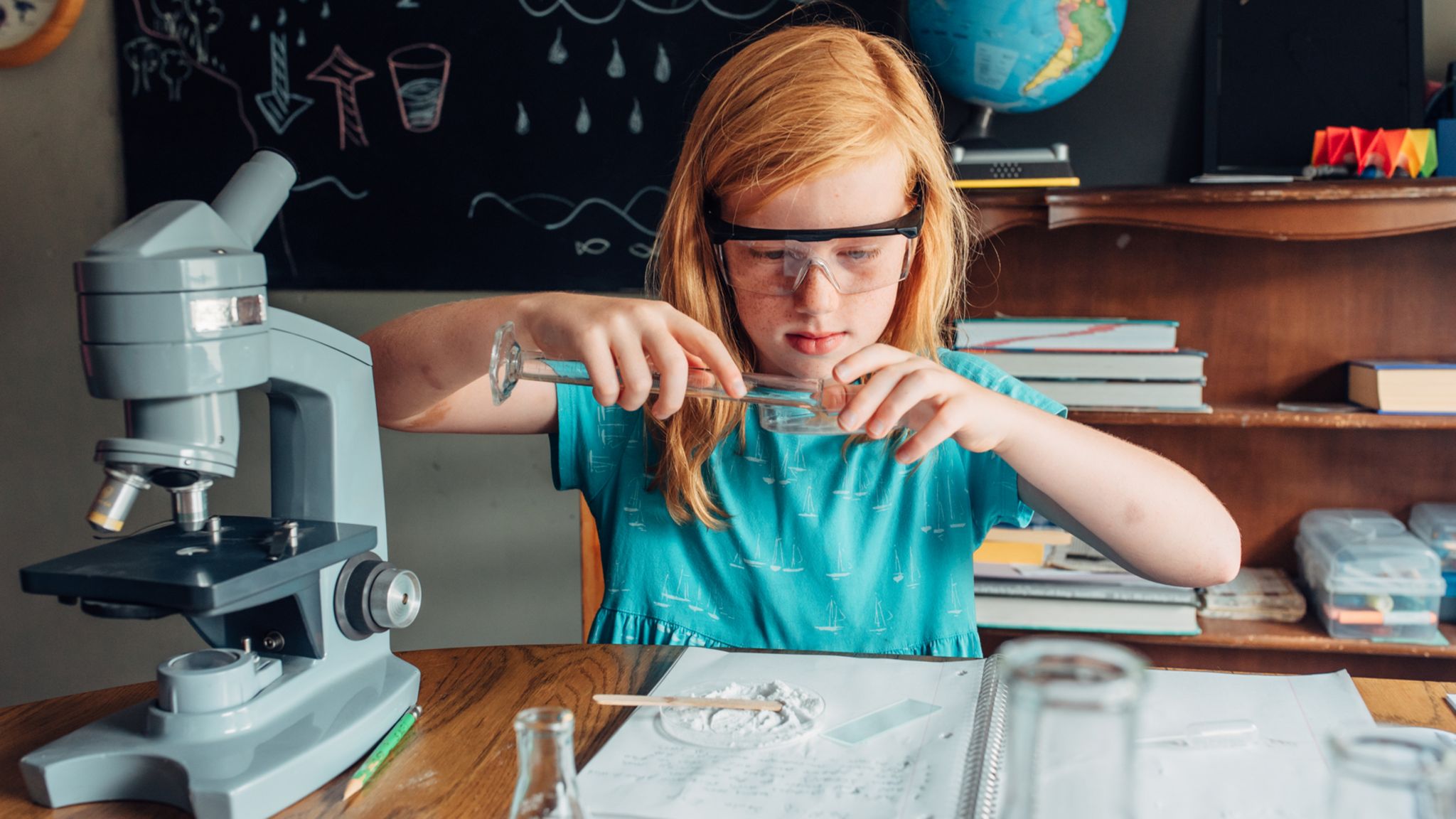 Ein Mädchen vor einer Schultafel mit Reagenzglas in der Hand