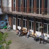 Im Innenhof der Schule sitzen fünf Menschen in der Sonne und rauchen