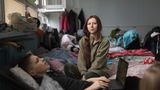 Eine junge Frau sitzt auf einem Bett, davor liegt ein Junge mit einem Laptop auf dem Schoß