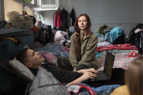 Eine junge Frau sitzt auf einem Bett, davor liegt ein Junge mit einem Laptop auf dem Schoß