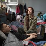 Eine junge Frau sitzt auf einem Bett, davor liegt ein Junge mit einem Laptop auf dem Schoß