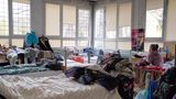 Eine alte Frau sitzt auf einem Bett in einem der Schlafzimmer und schaut aus dem Fenster