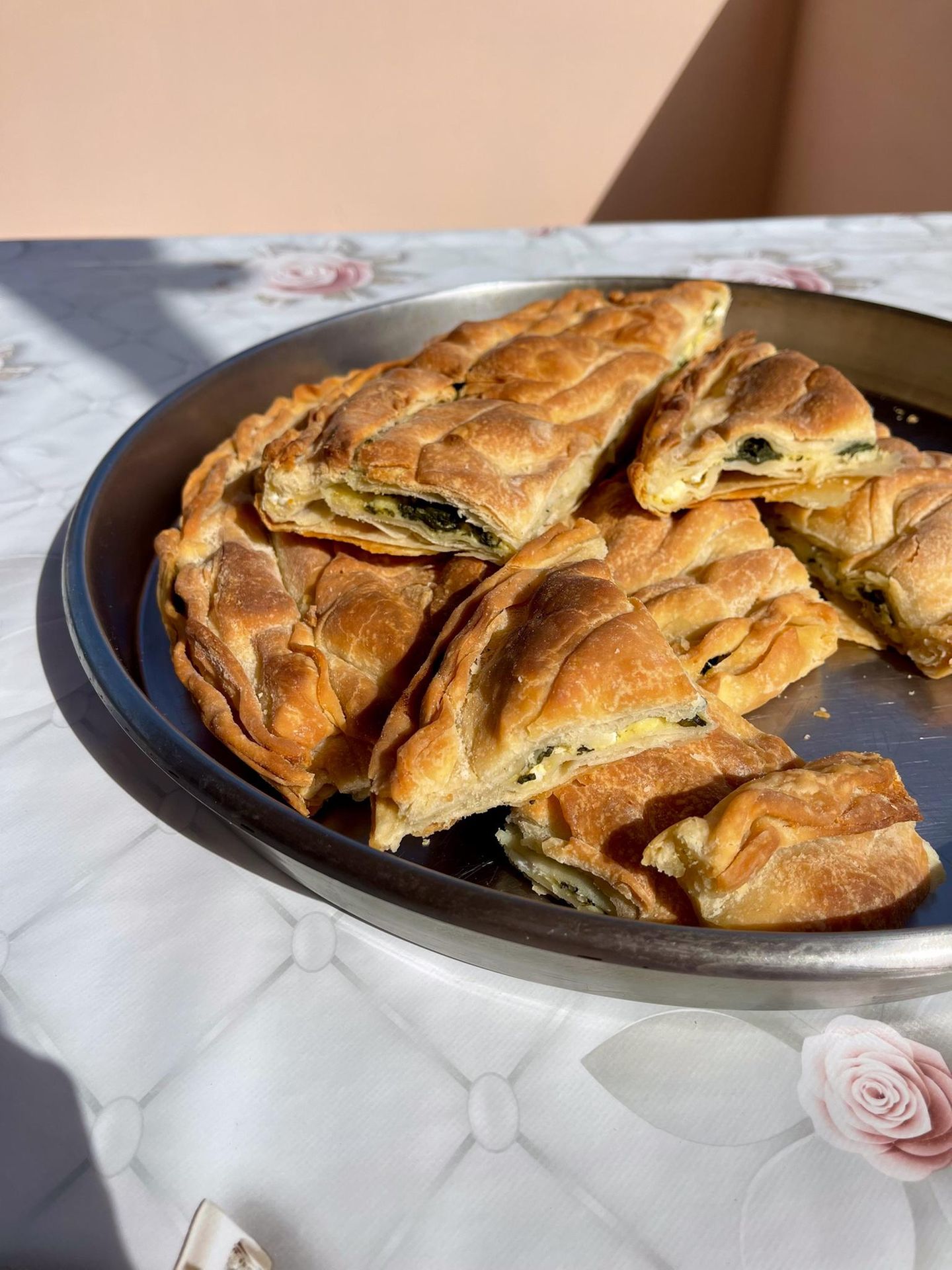 Spinatpita     "Die Spanakopita ist keine Festtagsspeise, sondern unser tägliches Brot", sagt Eleni, während sie den Filoteig hauchzart ausrollt. "Wenn die Kinder von der Schule kamen oder die Männer von den Feldern, war oft keine Zeit für aufwendige Gerichte. Aber eine Spinatpita – die konnte man schon am Morgen vorbereiten, und sie schmeckt warm genauso gut wie kalt. In den kargen Wintermonaten, wenn nicht viel auf den Feldern wuchs, war wilder Spinat unsere Rettung. Wir Frauen gingen gemeinsam sammeln, und aus dem, was die Natur uns schenkte, machten wir dieses einfache, aber nahrhafte Gericht."     Zutaten:1 kg frischer Spinat, gewaschen und grob gehackt1 Bund Frühlingszwiebeln, in feine Ringe geschnitten3 EL frischer Dill, gehackt2 EL frische Petersilie, gehackt300 g Feta-Käse, zerbröckelt3 Eier, leicht verquirlt3 EL Olivenöl, plus extra zum BestreichenSalz und frisch gemahlener schwarzer Pfeffer1 Prise frisch geriebene Muskatnuss450 g Filoteig (ca. 12-14 Blätter)100 g Butter, geschmolzen  1 EL Sesamsamen zum Bestreuen     Zubereitung:Den Backofen auf 180°C vorheizen.Den gewaschenen Spinat in eine große Pfanne geben und ohne zusätzliches Wasser bei mittlerer Hitze zusammenfallen lassen, gelegentlich wenden. In ein Sieb gießen und mit dem Rücken eines Löffels gut ausdrücken, um überschüssige Flüssigkeit zu entfernen.Den Spinat in eine große Schüssel geben und mit den Frühlingszwiebeln, Dill, Petersilie, zerbröckeltem Feta, Eiern und 3 EL Olivenöl vermischen. Mit Salz, Pfeffer und Muskatnuss abschmecken.Eine rechteckige Auflaufform (ca. 30 x 40 cm) mit etwas Olivenöl ausstreichen.Die Filoteigblätter auspacken und mit einem feuchten Tuch abdecken, damit sie nicht austrocknen.Die Hälfte der Filoteigblätter einzeln in die Form legen, jedes Blatt mit geschmolzener Butter bestreichen. Die Blätter sollten über den Rand der Form hängen.Die Spinat-Feta-Mischung gleichmäßig auf dem Filoteig verteilen.Die restlichen Filoteigblätter einzeln darüber legen, jedes Blatt wieder mit Butter bestreichen. Die überhängenden Teigränder nach innen falten und ebenfalls mit Butter bestreichen.Die Oberfläche mit einem scharfen Messer vorsichtig in Rauten- oder Quadratform einschneiden (nicht ganz durchschneiden). Mit Sesamsamen bestreuen.Im vorgeheizten Ofen ca. 45-50 Minuten backen, bis die Oberfläche goldbraun und knusprig ist.Vor dem Servieren etwa 15 Minuten abkühlen lassen und dann entlang der vorgeschnittenen Linien in Stücke schneiden.