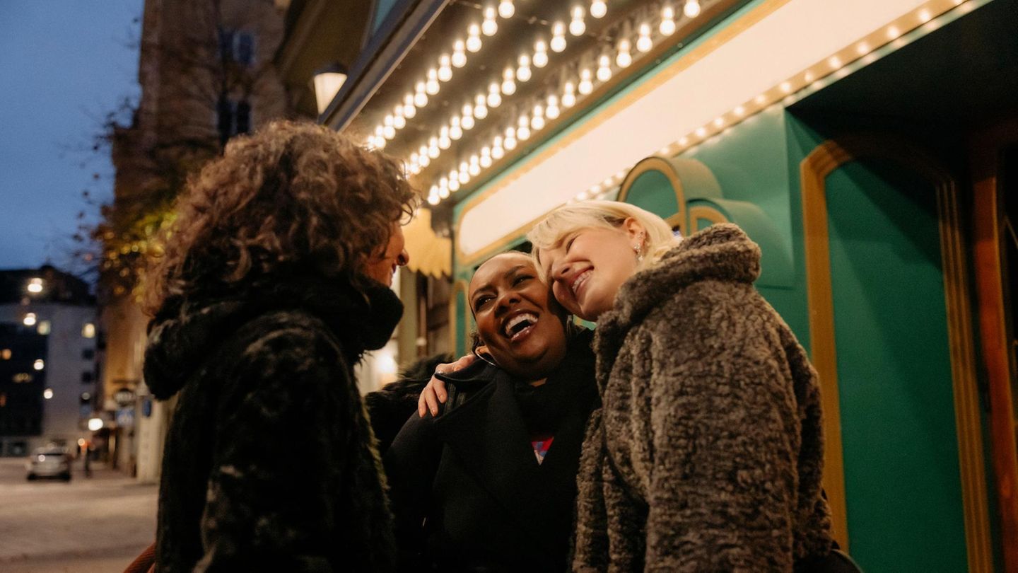 Drei Frauen stehen vor einem Lokal in der Dämmerung und lachen