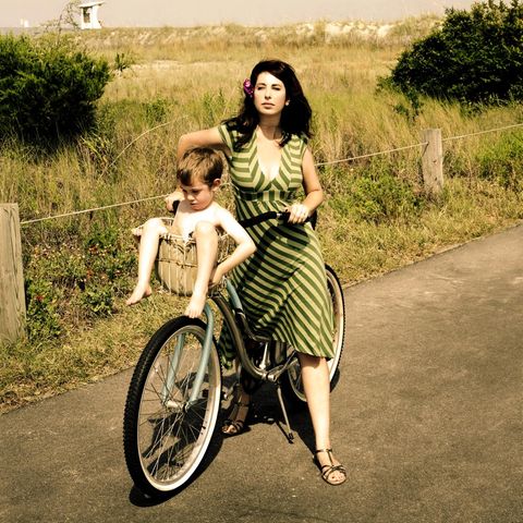 Mothers' pension. Woman in a retro look transports her son in a bicycle basket