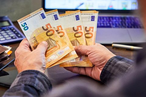 Nettogehalt Symbolbild: Mann zählt am Laptop 50-Euro-Scheine