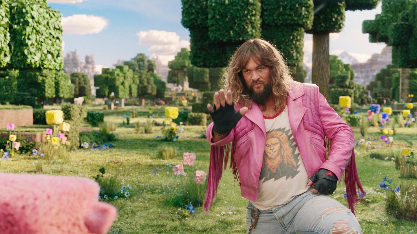 Jason Momoa in einer rosa Jacke streckt im Minecraft Movie die Hand nach vorn aus