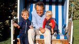 Mann in einem im einem Garten aufgestellten Strandkorb, auf seinem Schoß sitzen zwei kleine Kinder