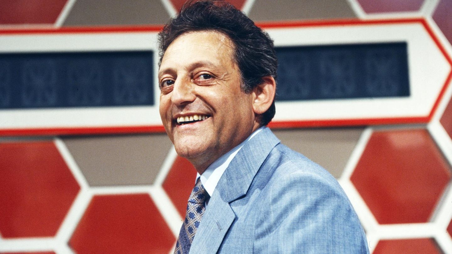 Quizmaster Hans Rosenthal lacht, gekleidet in ein blaues Jackett, in die Kamera